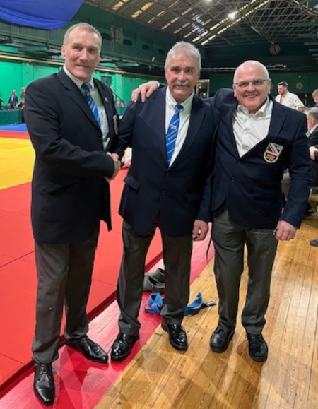 3 Judo referees stood next to each other. 2 congratulating Peter Kelly (centre)